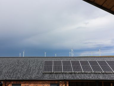 View of solar panels on a roof with wind turbines and clouds at The Gavel in Morpeth
