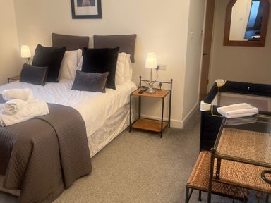 A bedroom with a bed, side table, lamp, and a cot at 4 Bickington Road Barnstaple