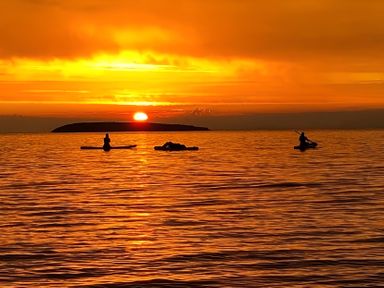 A sunset over the ocean with kayakers at Blue Haven in Penmaenmawr