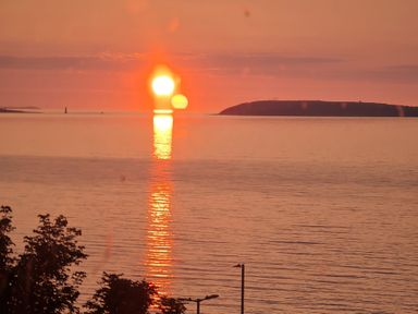 A sunset over the ocean with an island and lighthouse at Sea View Escape in Penmaenmawr