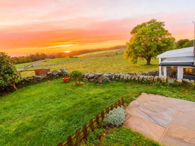 A garden with a stone wall and patio during sunset at 1 Sunny Brae Embleton