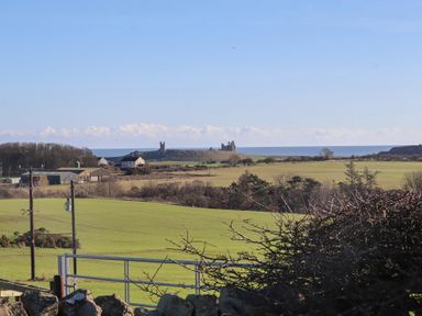 A view of fields and a castle by the sea at Harry's Cottage in Embleton