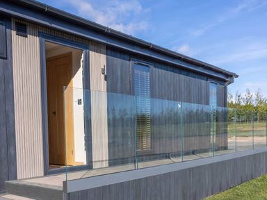 An exterior view of a lodge with glass railing and door at Isca Lodge - With Decking - Lodge 1 in Wombleton