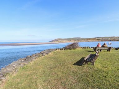 A view of water and hills with two people seated on benches at Ty Gwartheg Newport