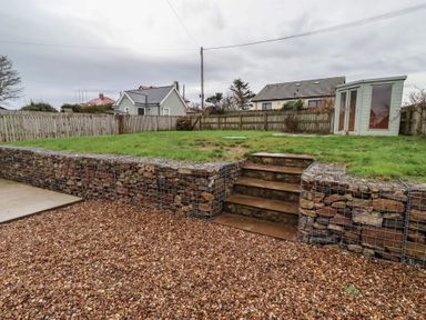 A garden with a stone wall and steps at Braeburn in Bamburgh
