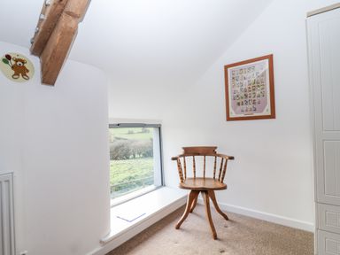 An attic room with a chair and window at Dairy Cottage Bullhornstone near South Brent