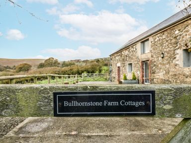 Sign for Bullhornstone Farm Cottages with cottages and hills in the background at Dairy Cottage Bullhornstone near South Brent