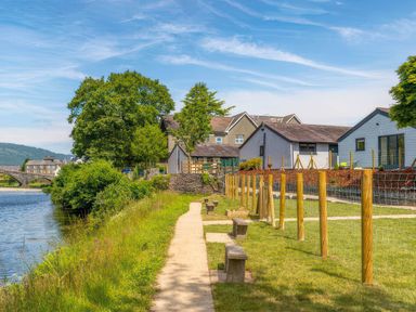 A path alongside a river with benches and buildings at Aspen Apartment in Llanrwst