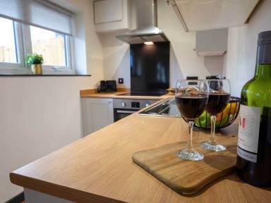 A kitchen with wine glasses and a bottle on a wooden surface at Ash Cottages in Llanrwst