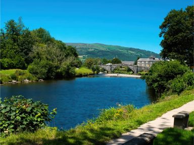 A river with a stone bridge and a pathway at Ash Cottages Llanrwst