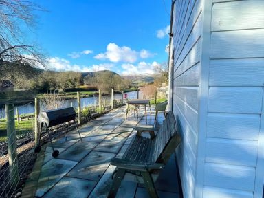 An outdoor area with a grill and seating near a river at River View Cottage in Llanrwst