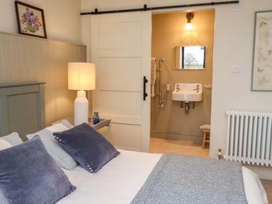 A bedroom featuring a bed, lamp, and a bathroom area with a sink at Fairview in Darsham