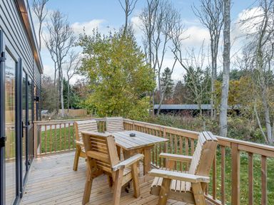 A deck with wooden furniture and trees at Anderby Spa (Pet) in Louth