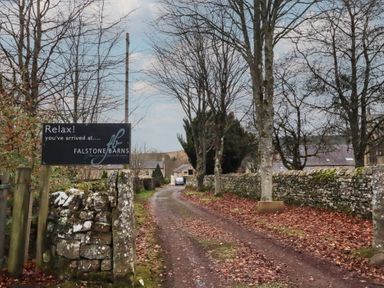 A sign indicating arrival at Falstone Barns with trees and a road in Hexham