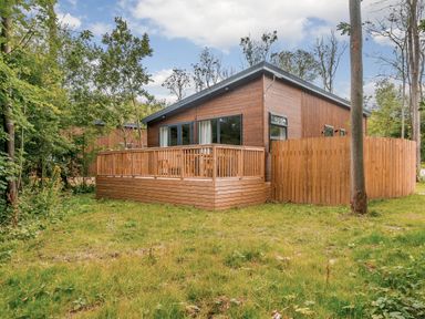 A house with a wooden deck and fence surrounded by grass and trees at Stamford Spa in Louth