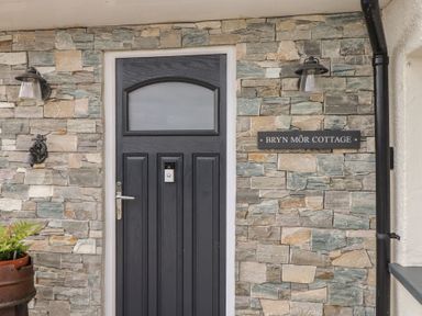 The entrance door with a stone wall and a sign at Bryn Môr Cottage in Mynytho near Llanbedrog