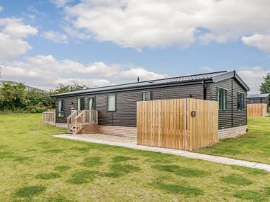 A wooden cabin with a fence and grassy area at Brayford Lodge Spa in Louth