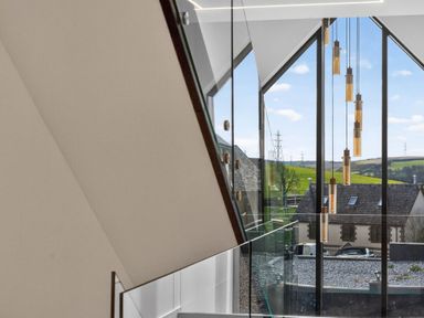 A staircase with glass railing and hanging light fixtures at Heddfan in Carmarthen