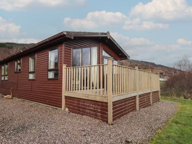 A wooden cabin with a deck and gravel area at Monach 1