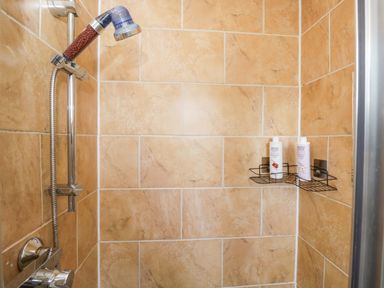 A shower with a metal shelf holding shampoo bottles at Lady Of Lourdes in Whitchurch, Herefordshire
