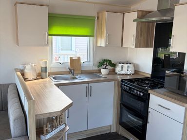 A kitchen with cabinets, sink, stove, and appliances at The Beachside Hideout - St Michaels Caravan Park, Towyn
