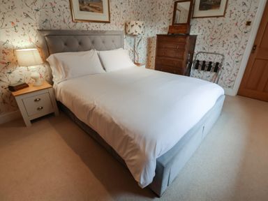 A bedroom with a bed, side table, lamp, and chest of drawers at Winston Lodge in Beccles