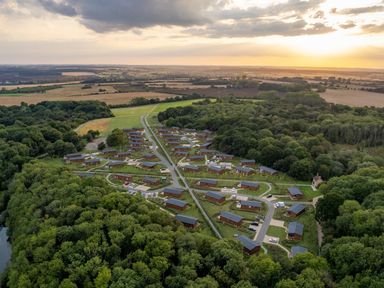 An aerial view of a cabin site surrounded by trees and fields at The Wansford in Kings Cliffe