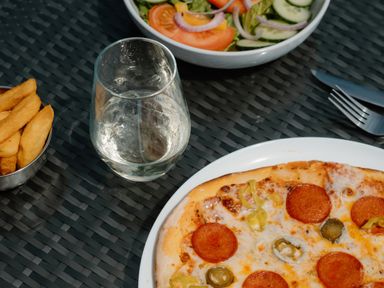 A pizza with toppings, a glass of water, a salad and fries in an outdoor dining area at The Wansford in Kings Cliffe