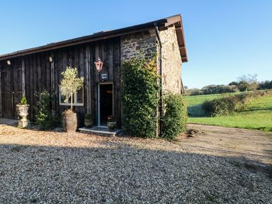 A wooden building with a stone wall and plants at Lake View in Crediton