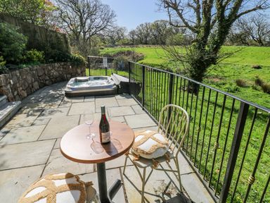 An outdoor patio with a hot tub and a table with a wine bottle and glasses at Rose Apartment in Old Walls, Llanrhidian, Gower