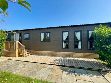 An exterior view of a cabin with a wooden deck at Acacia Waterside Spa Carlton Miniott near Thirsk