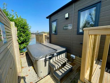 An outdoor area with a hot tub, decking, and a building at Acacia Waterside Spa Carlton Miniott near Thirsk