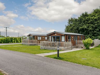 Two wooden chalets with decking in an outdoor area at Alder Spa in Carlton Miniott near Thirsk
