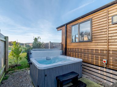 A hot tub next to a wooden cabin at Alder Waterside Spa Carlton Miniott near Thirsk