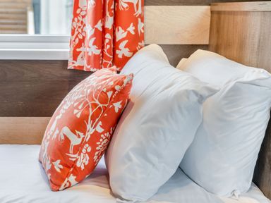 A bed with white pillows and an orange patterned cushion at Kinder Spa Carlton Miniott near Thirsk
