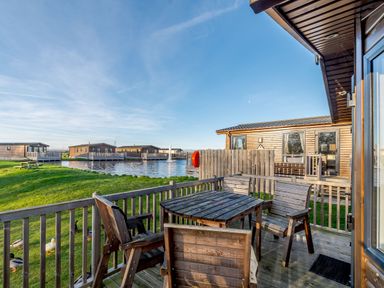 An outdoor area with a wooden table and chairs near the water at Alder Waterside Spa (Pet) Carlton Miniott near Thirsk