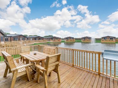 An outdoor area with a wooden table and chairs overlooking a pond at Spindle Spa Carlton Miniott near Thirsk