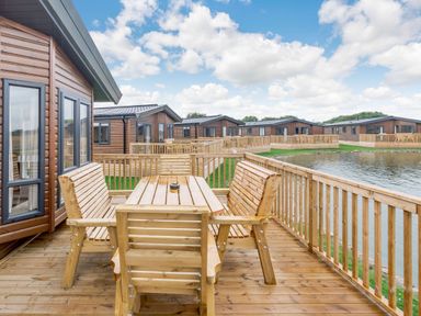 An outdoor area with a wooden table and chairs overlooking a lake at Spindle Spa Carlton Miniott near Thirsk