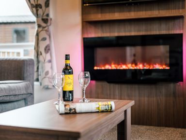 A living room with a wine bottle and glasses on a coffee table at Larch Waterside Spa Carlton Miniott near Thirsk