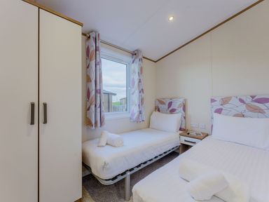 A bedroom with two beds, a wardrobe, and a window at Larch Waterside Spa (Pet) Carlton Miniott near Thirsk
