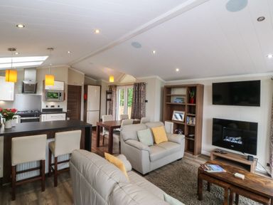 A living room with a sofa and kitchen area at Plas Marchog Lodge in Rhoscefnhir near Pentraeth