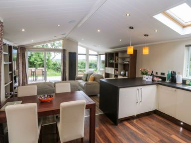 A living room with sofa and dining area at Plas Marchog Lodge Rhoscefnhir near Pentraeth