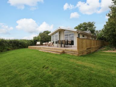An outdoor area with a lodge and deck seating at Plas Marchog Lodge in Rhoscefnhir near Pentraeth