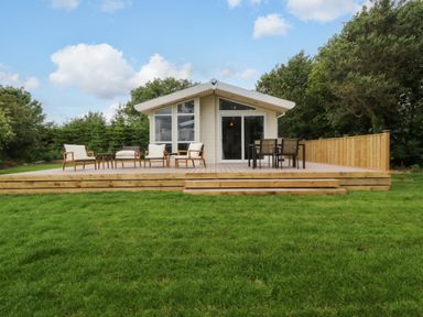 A house with a deck and chairs at Plas Marchog Lodge near Rhoscefnhir Pentraeth