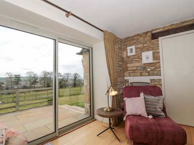 A living room with an armchair and sliding doors at Daisy Bank in Maugersbury near Stow-On-The-Wold