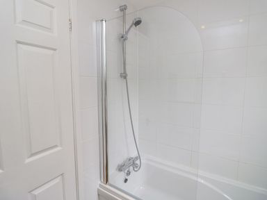 A bathtub with shower and wall tiles at Harbour View Poole