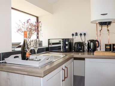 A kitchen with a sink, wine bottle, and microwave at Lannlyvri Lodge in Lanlivery near Lostwithiel