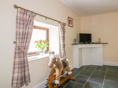 A living room with a rocking horse and television at Camellia Cottage in Bodmin