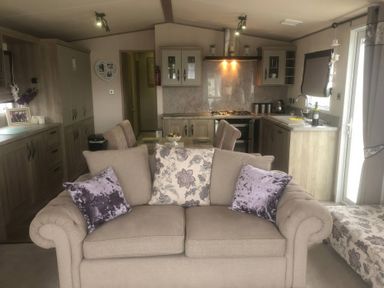 A living room with a sofa and kitchen area at 62 Guddlebeck, Lakeland Leisure Park, Flookburgh