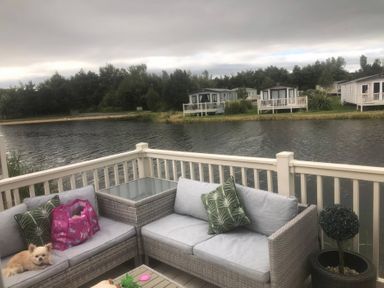 An outdoor seating area with a sofa and a lake view at 62 Guddlebeck in Lakeland Leisure Park, Flookburgh